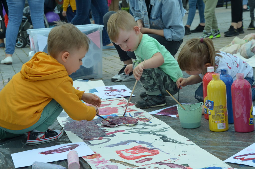 Na obrazku dzieci malują na kartce papieru
