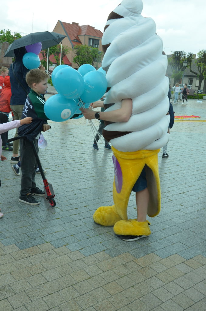 Na obrazku jest maskotka lód obdarowująca dzieci gadżetami balonami