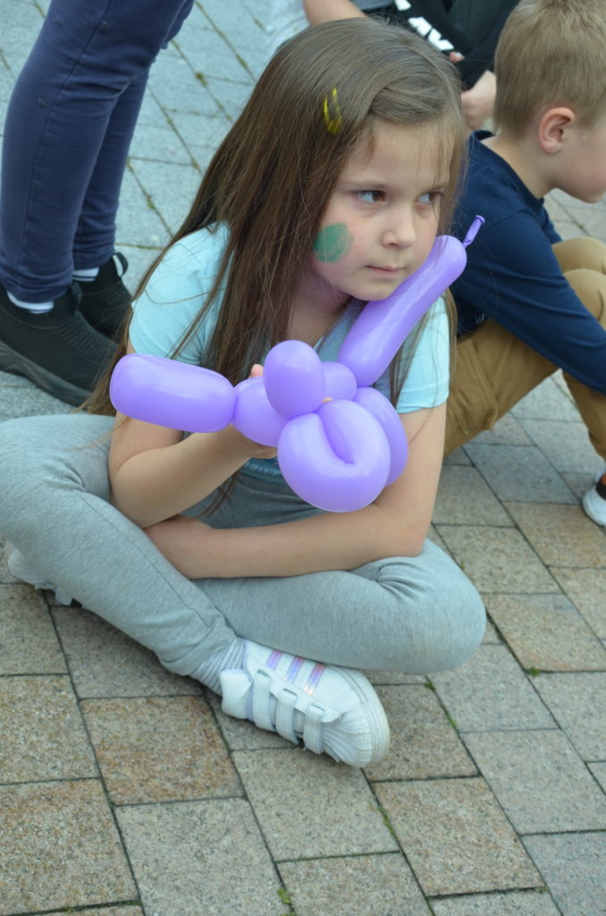 na obrazku siedzi dziewczynka z balonowym zwierzątkiem