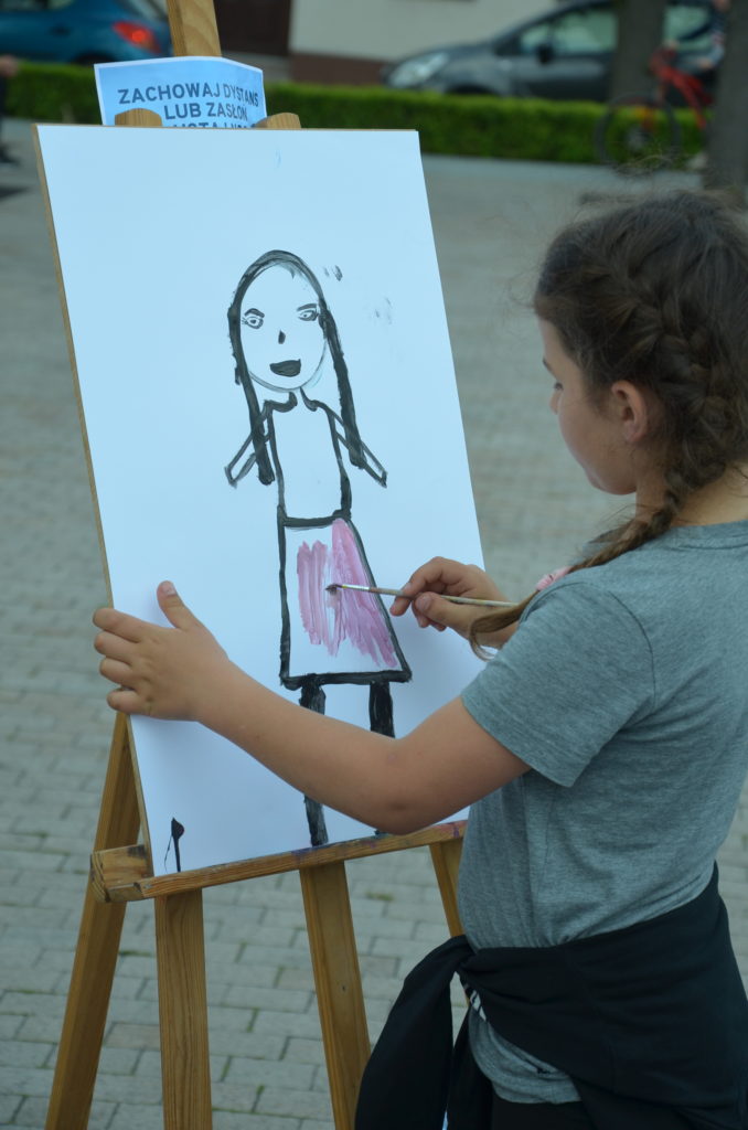 Na obrazku dziewczynka maluje na sztaludze