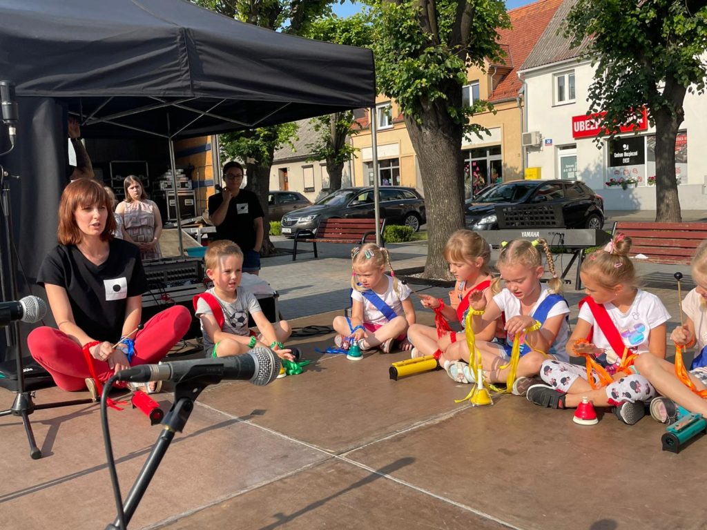 Na obrazku grupa dzieci wraz z kobietą siedzi na scenie