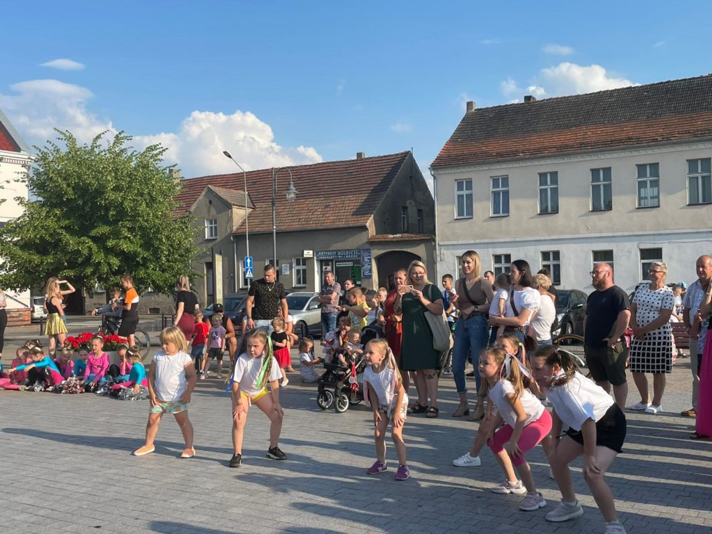 Na obrazku tańczy grupa dzieci, a za nią stoją dorośli
