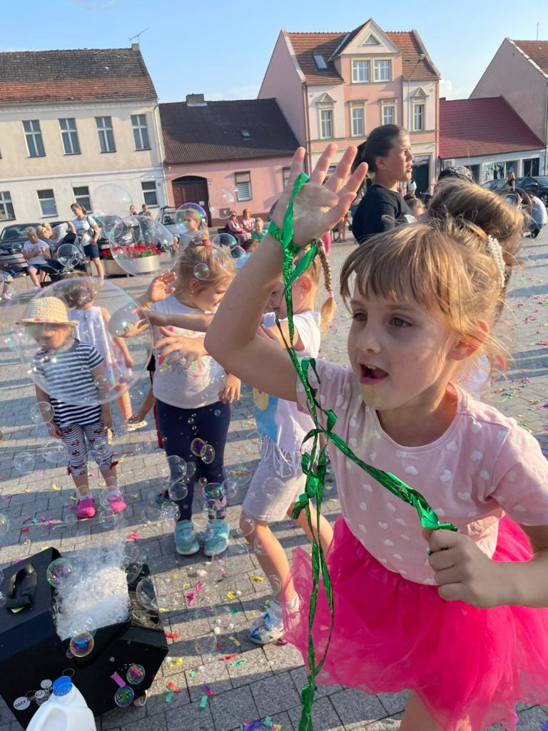 Na obrazku grupa dzieci bawi się bańkami mydlanymi