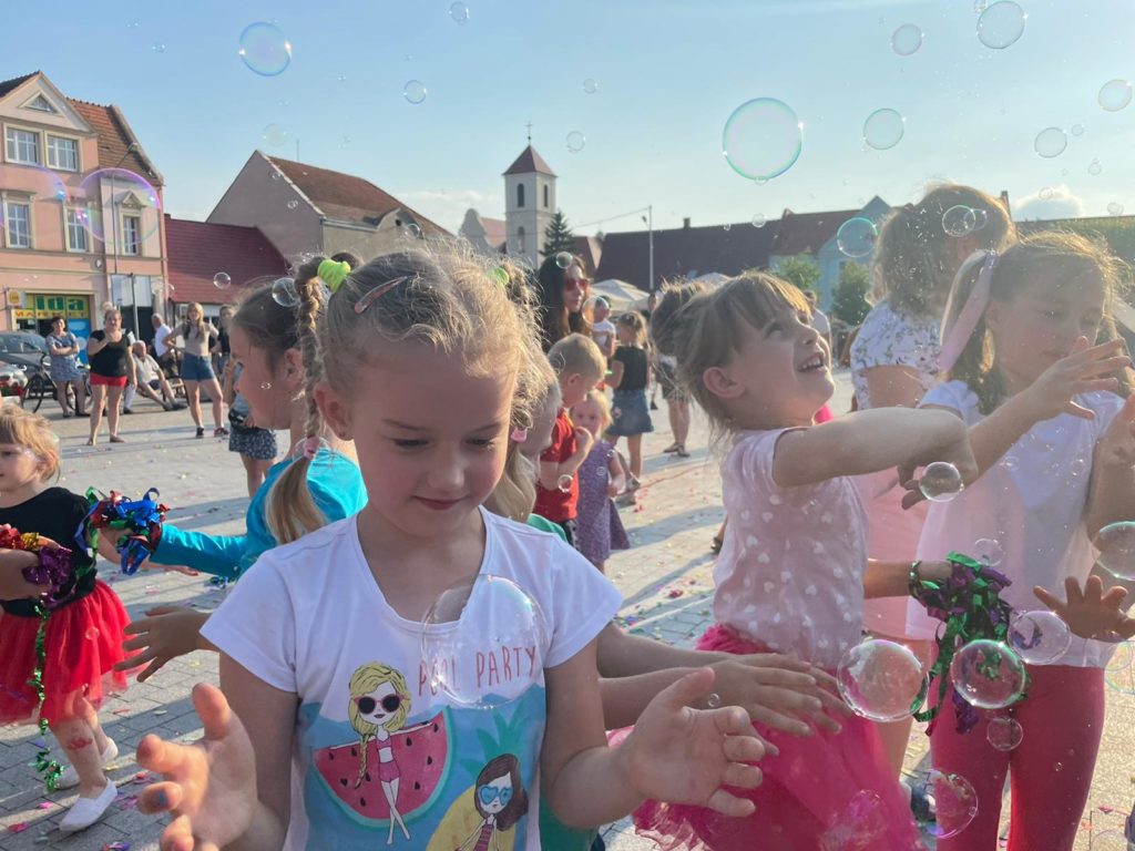 Na obrazku grupa dzieci bawi się bańkami mydlanymi