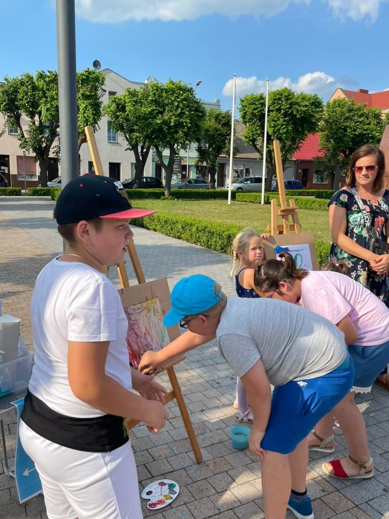Na obrazku grupa dzieci maluje na sztaludze