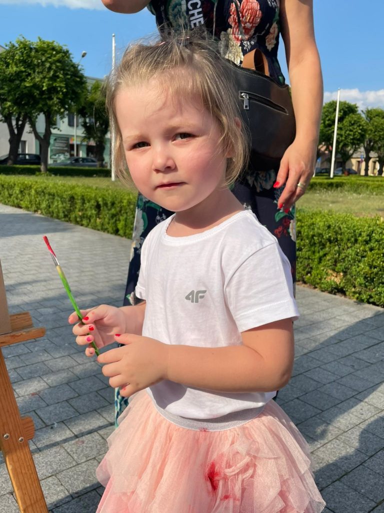 Na obrazku dziewczynka maluje na sztaludze