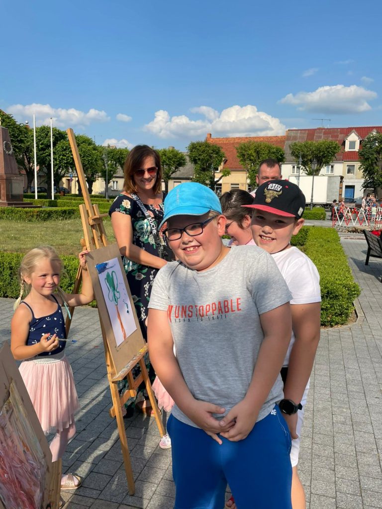Na obrazku grupa dzieci stoi przy sztalugach