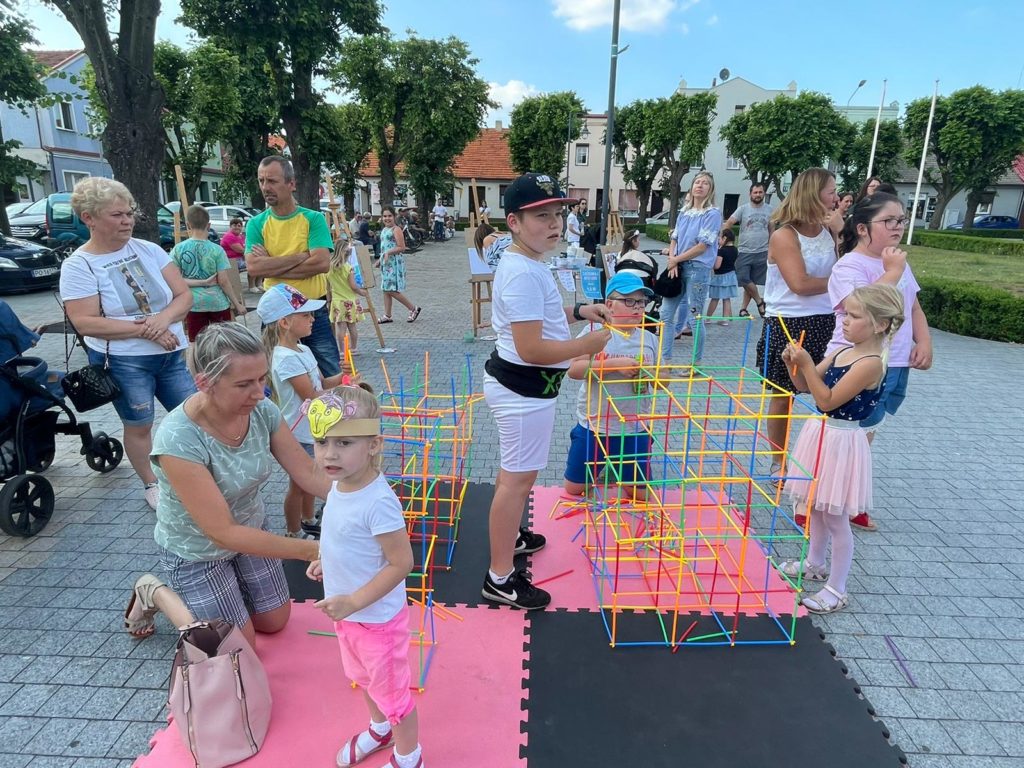 Na obrazku dzieci i dorośli układają klocki-słomki