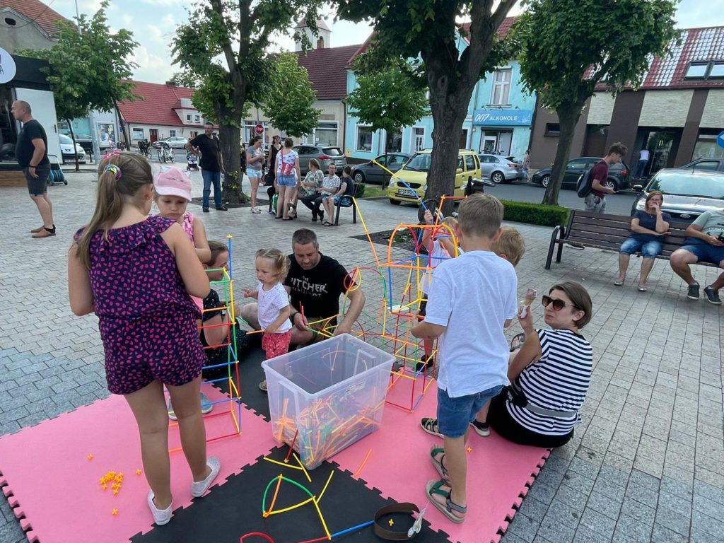 Na obrazku dzieci i dorośli układają klocki-słomki