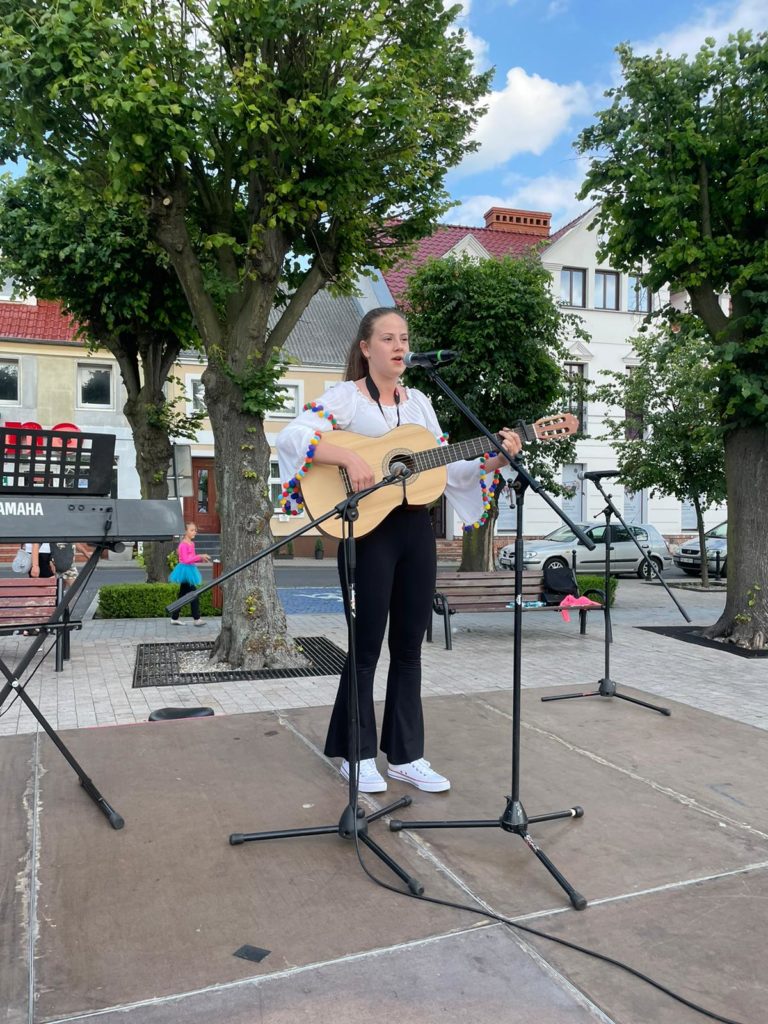 Na obrazku dziewczynka śpiewa i gra na gitarze