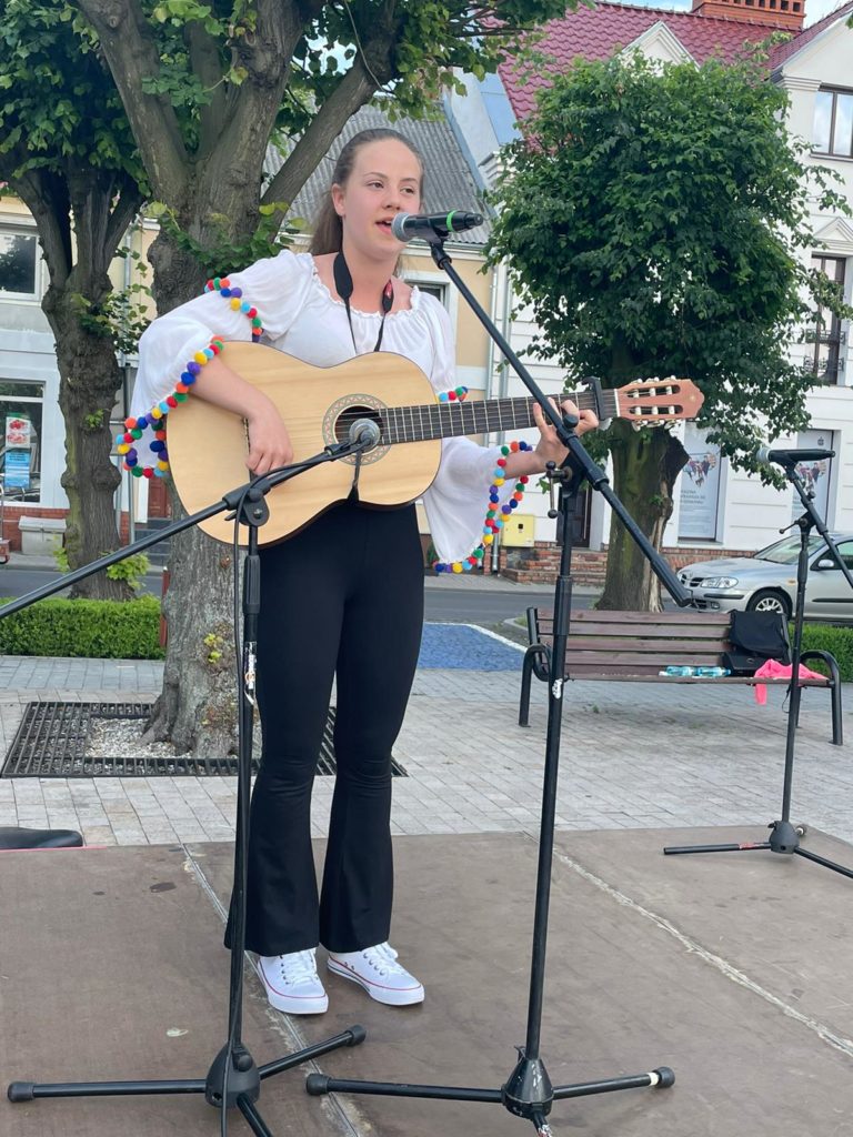 Na obrazku dziewczynka śpiewa i gra na gitarze