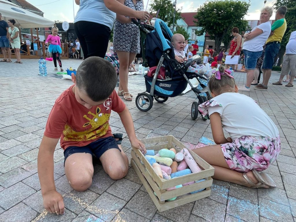 Na obrazku dzieci rysują kredą po bruku