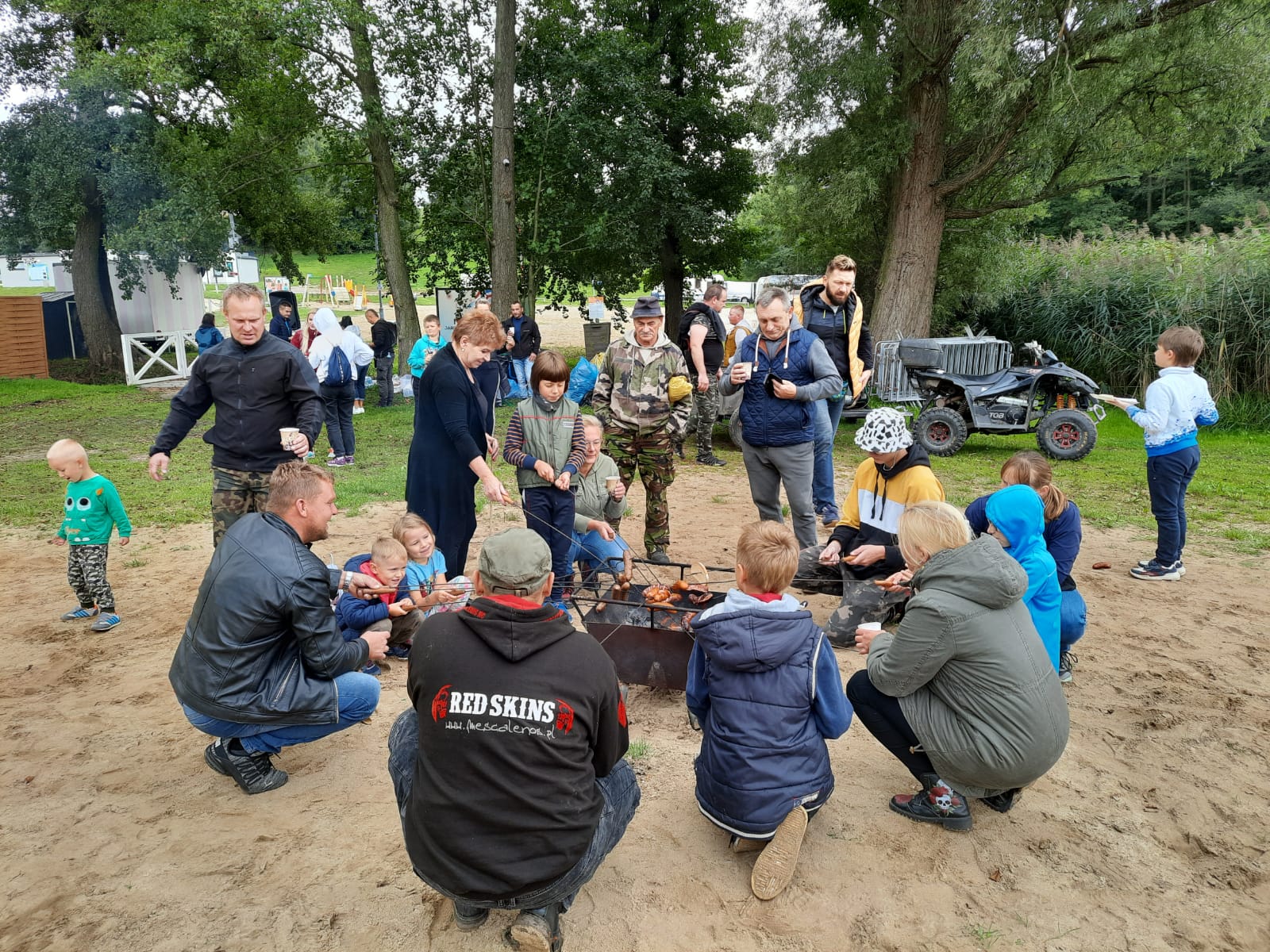 Zdjęcie przedstawia ludzi pieczących kiełbaski na ogniu.