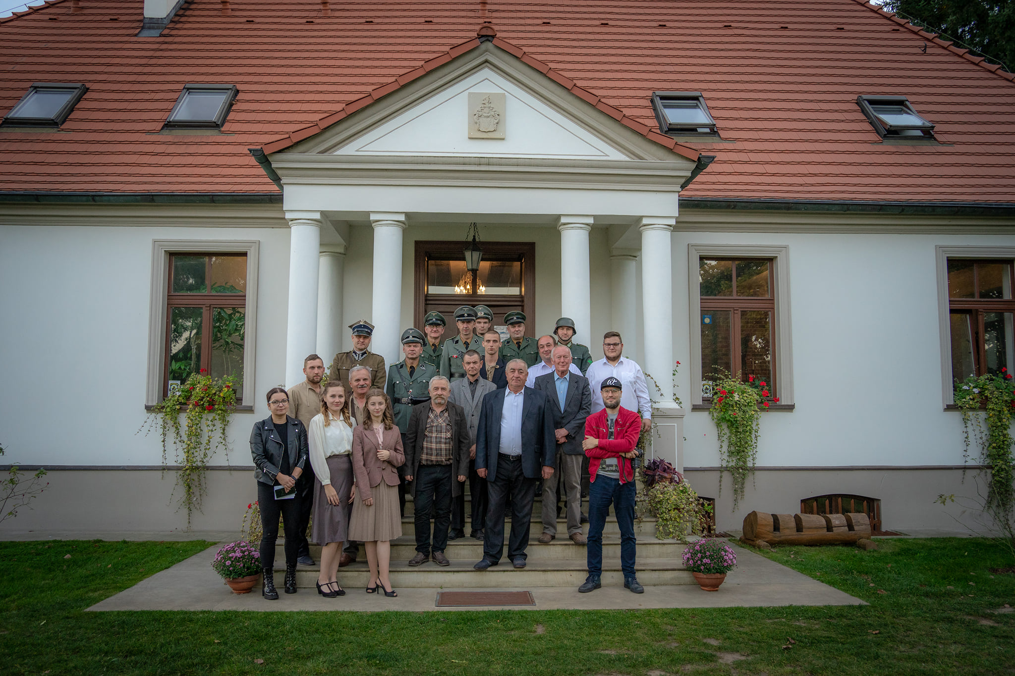 Zdjęcie przedstawia grupę ludzi przed dworkiem.